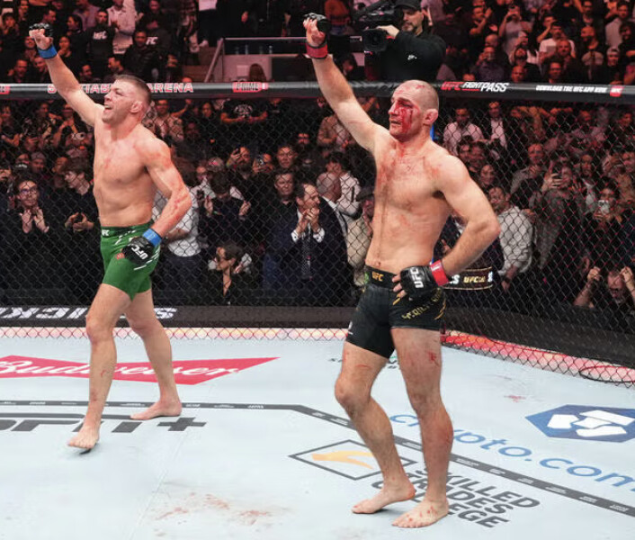 Two fighters raise their arms as the final horn sounds — the moment before the judges settle what the market could not